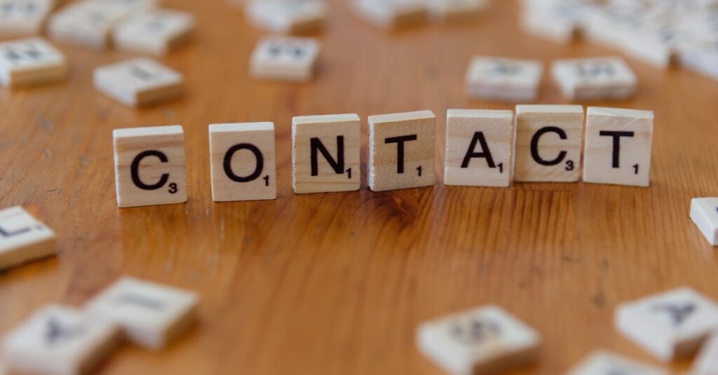 Scrabble letters spelling 'contact' on a wooden table surface.