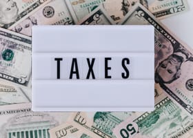 Top view of white vintage light box with TAXES inscription placed on stack of USA dollar bills on white surface