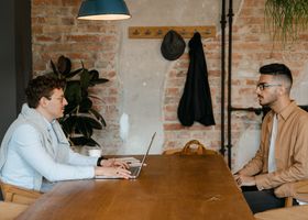 Two men in a modern office having a business discussion across a wooden table.