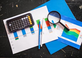Top view of financial charts with a smartphone calculator, magnifying glass, and pencils on a desk.